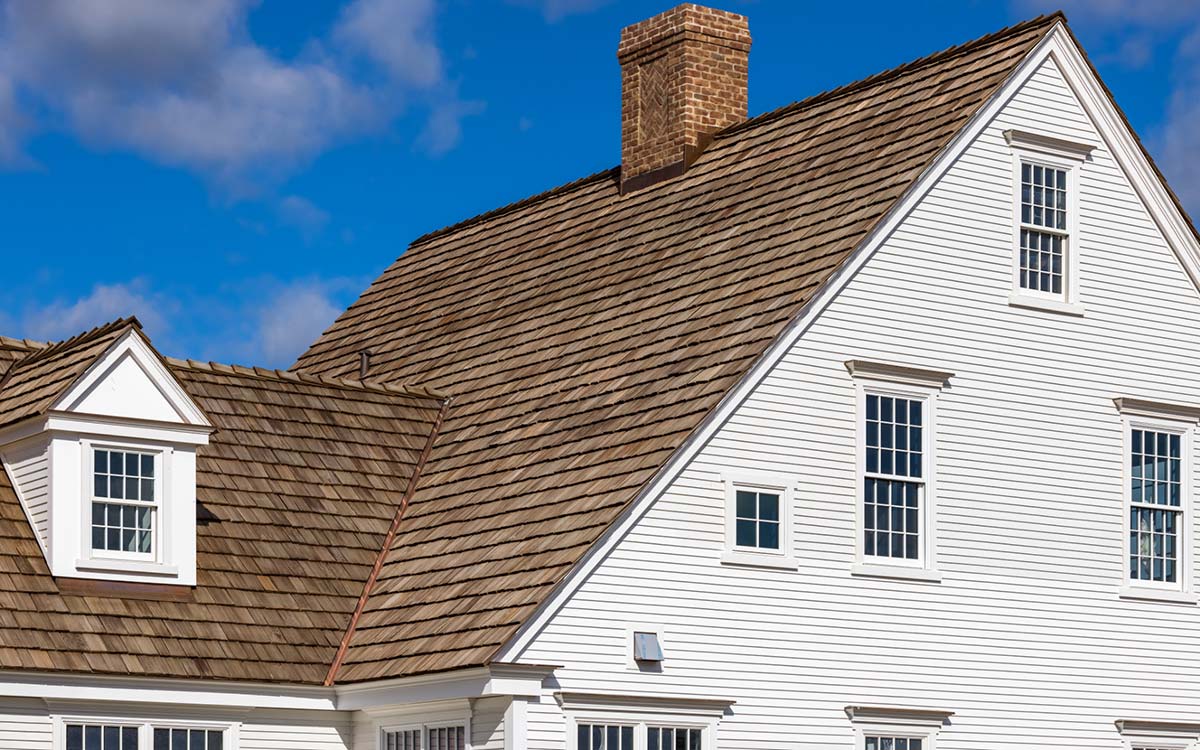 A classic white colonial-style home featuring a cedar shake roof and red brick chimney.