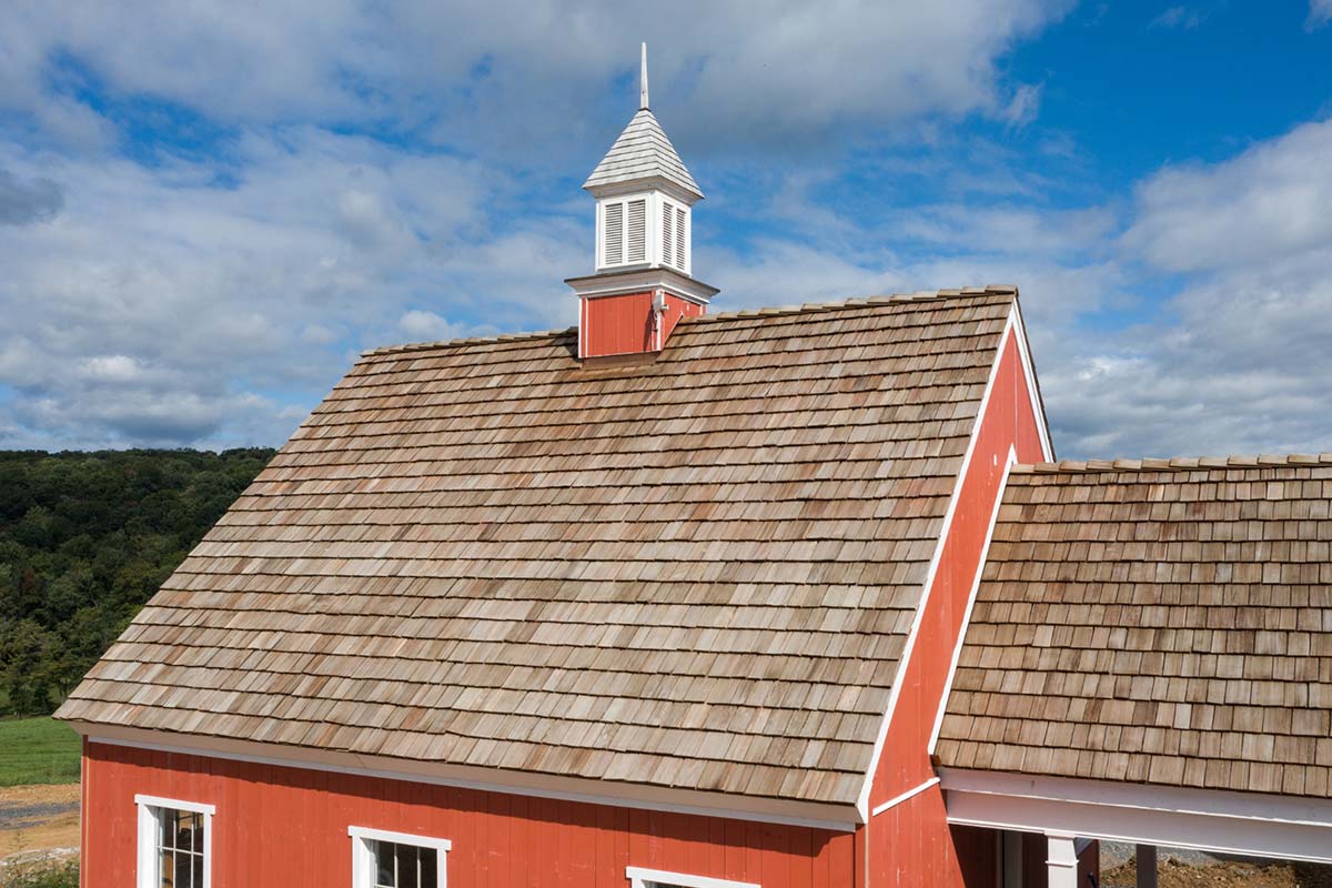 A red barn with a steep cedar shake roof and white trim under a partly cloudy sky.