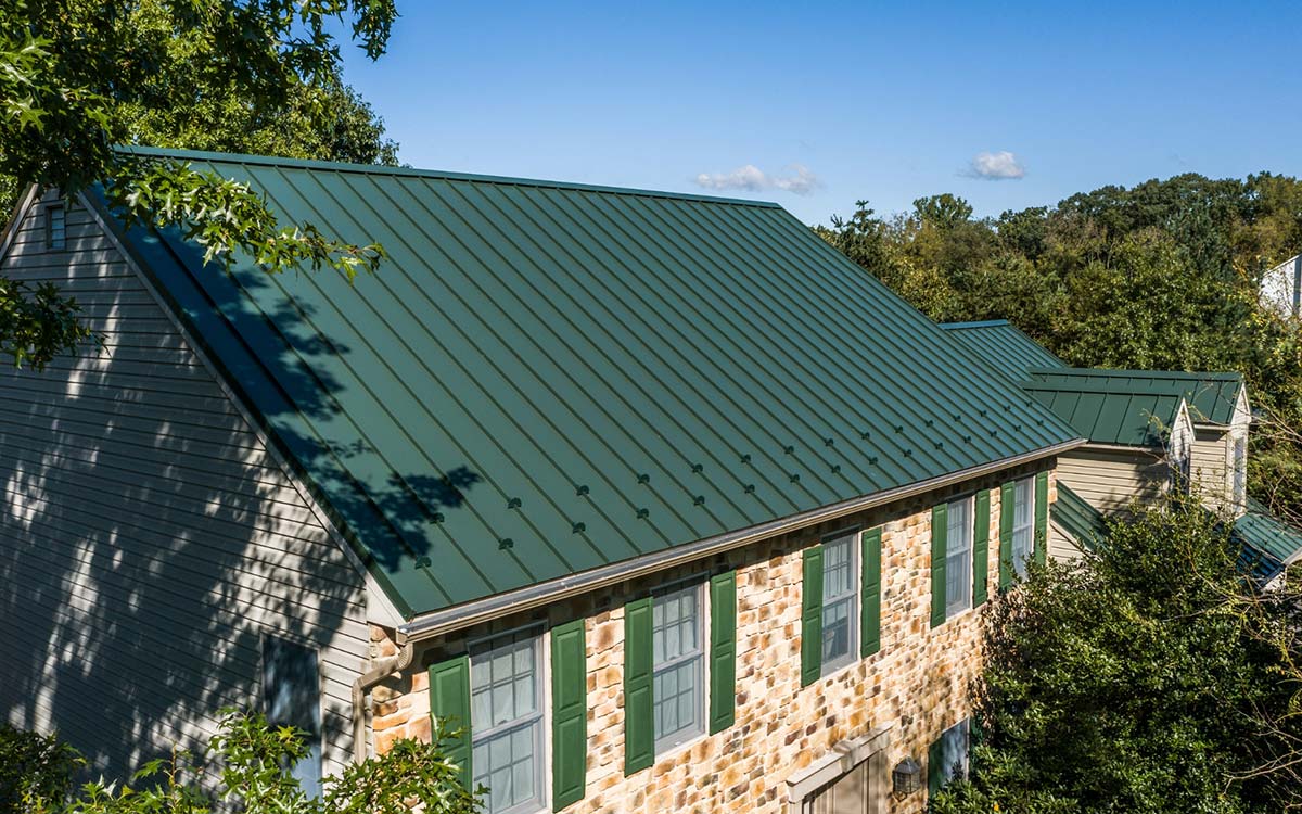 A house with a green standing seam metal roof and a mixed stone and siding exterior.